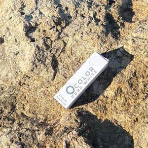 Ocolor Pure White cosmetic box on a textured natural stone surface in sunlight