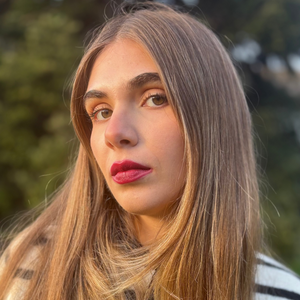 Woman with natural makeup, bold pink lipstick, and straight hair outdoors
