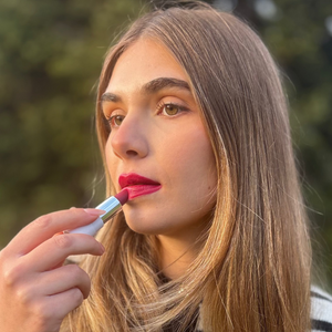 Woman applying natural vegan pink lipstick outdoors, close-up beauty makeup