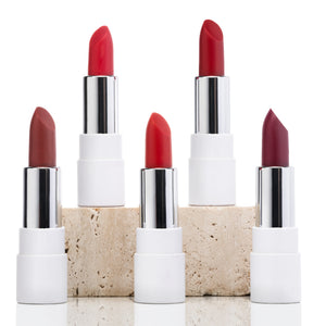 Five vegan lipsticks in white tubes, assorted shades of red, arranged on stone block
