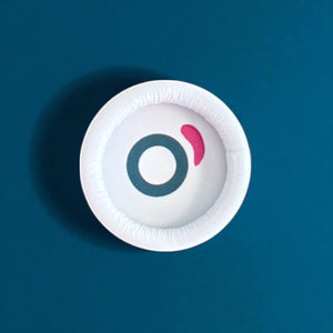 White round cosmetic container lid with teal and pink logo on blue background