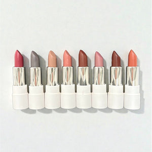 Eight natural vegan lipsticks in assorted shades with white cases on a light background
