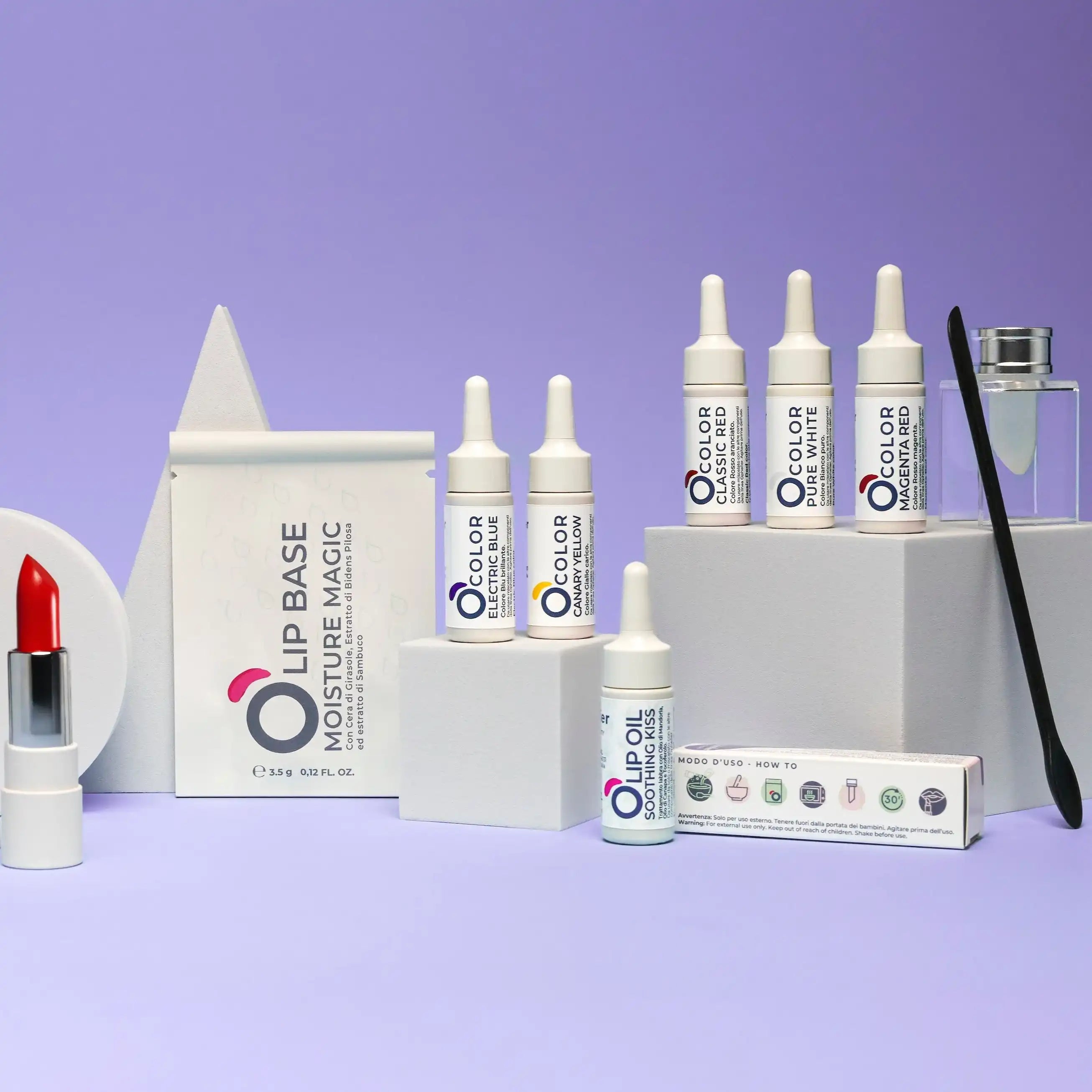 Vegan beauty products including red lipstick, lip base, color drops, and lip oil on a pastel display