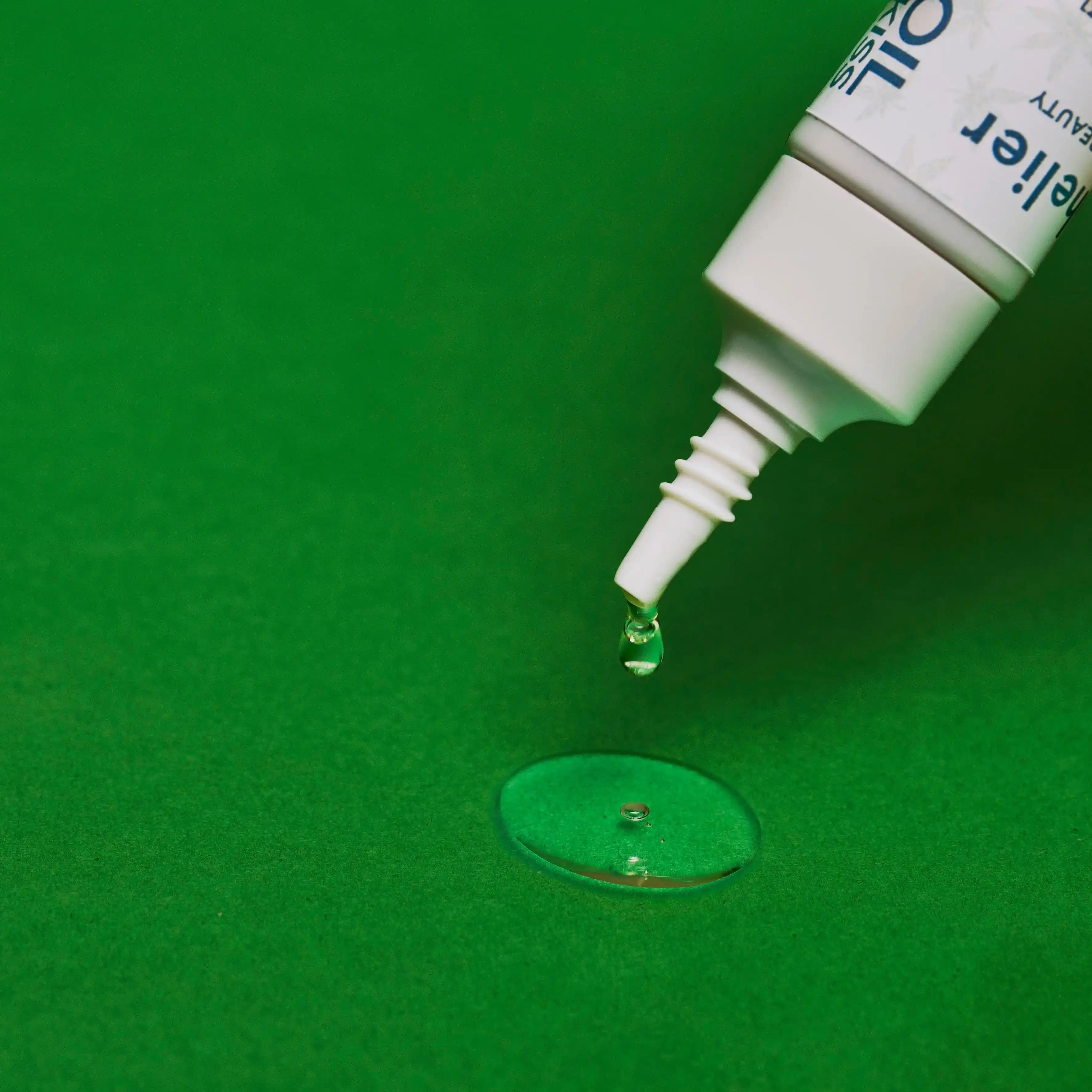 Drop of natural vegan serum from a white cosmetic tube on green background