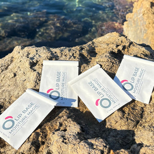 Lip Base Moisture Magic sachets on a rocky surface by the sea, natural vegan makeup product