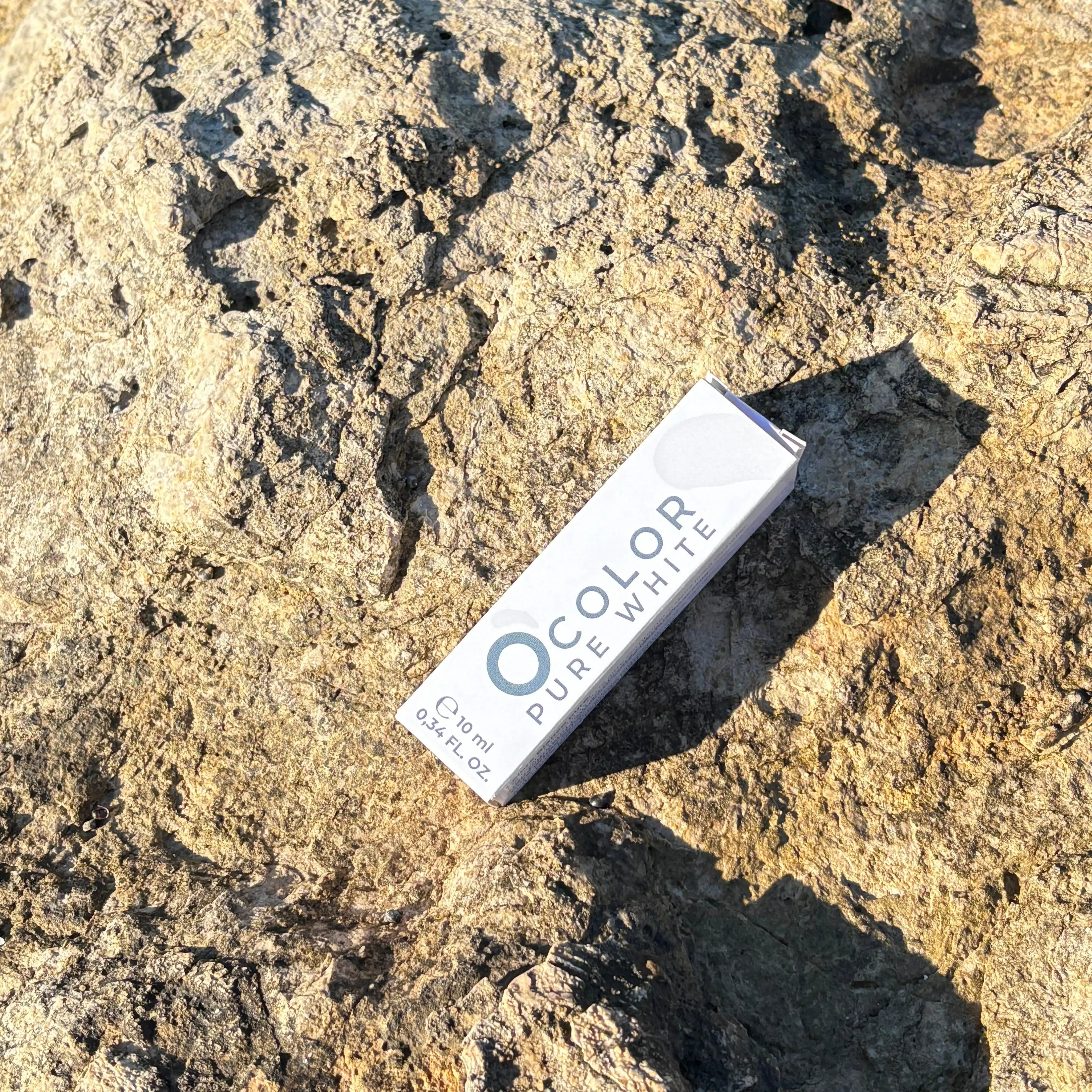 Ocolor Pure White cosmetic box on a textured natural stone surface in sunlight