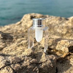 Clear cosmetic container with silver cap on rocky surface near water