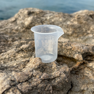 Clear plastic measuring cup for DIY cosmetics on rocky outdoor surface