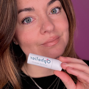 Woman with natural makeup holding custom beauty lipstick with a purple background
