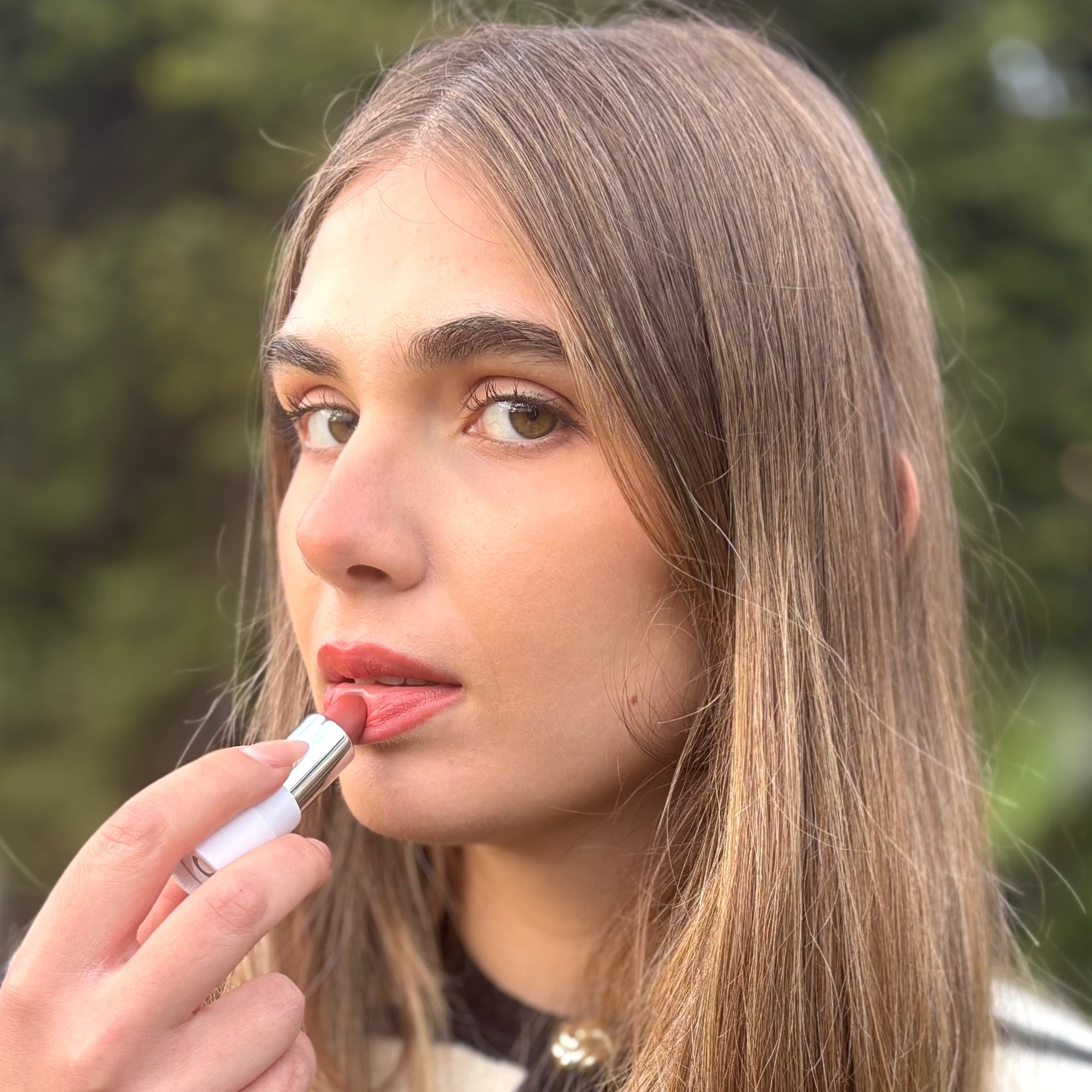 Woman applying natural vegan lipstick outdoors, close-up of lips and makeup