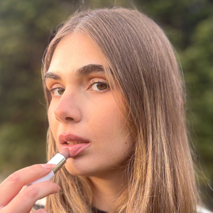 Woman applying natural vegan lipstick outdoors, close-up beauty portrait