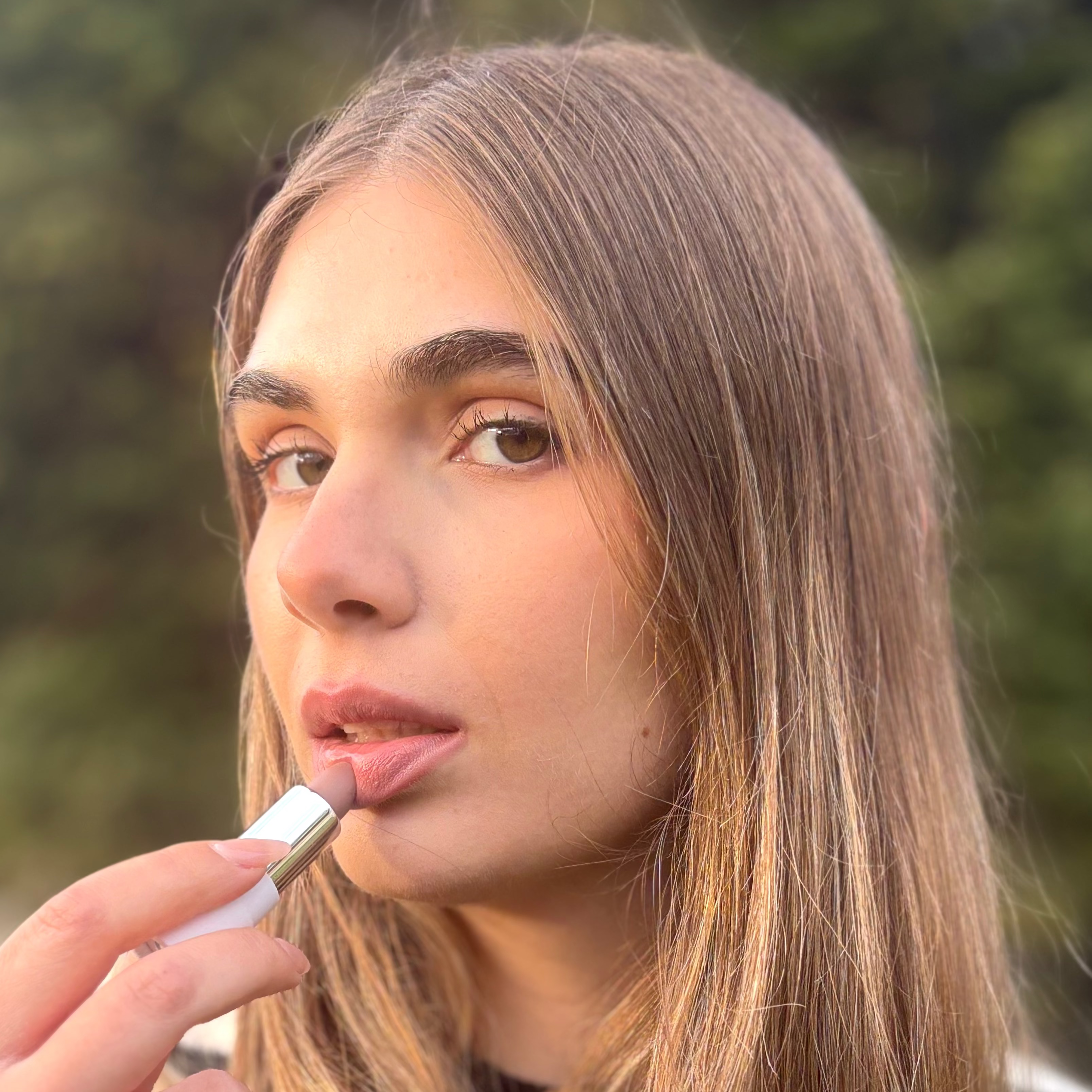 Woman applying natural vegan lipstick outdoors, close-up beauty portrait