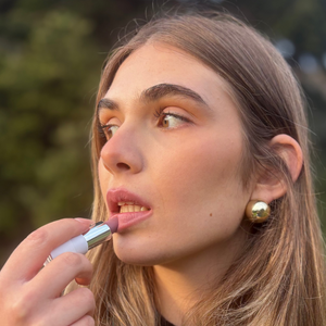 Woman applying natural vegan pink lipstick outdoors, close-up beauty makeup