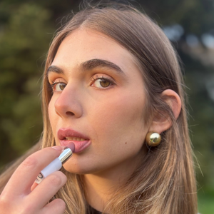 Woman applying vegan natural lipstick outdoors, close-up of fresh makeup look