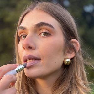Woman applying natural nude lipstick outdoors, close-up makeup focus