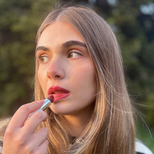 Woman applying natural vegan red lipstick outdoors with sunlight highlighting her face