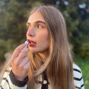 Woman applying natural vegan lipstick outdoors, long blonde hair, soft daylight