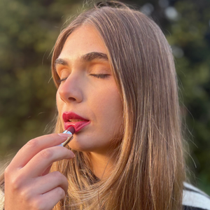 Woman applying natural vegan lipstick outdoors with closed eyes, soft daylight