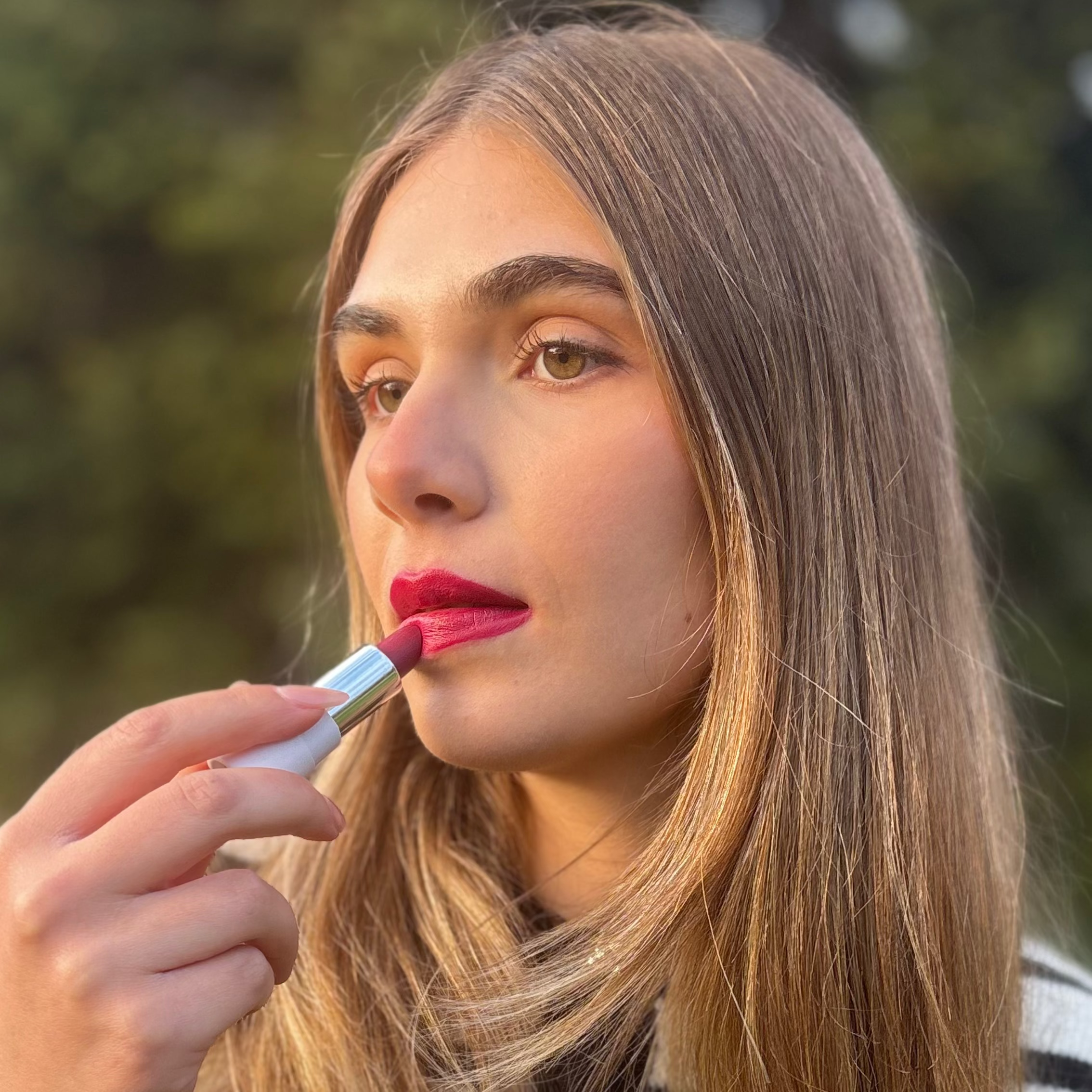 Woman applying natural vegan pink lipstick outdoors, close-up beauty makeup