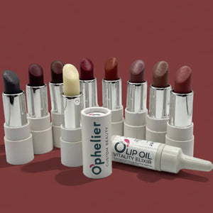 Assorted natural lipsticks and a lip oil elixir with white packaging on a mauve background.