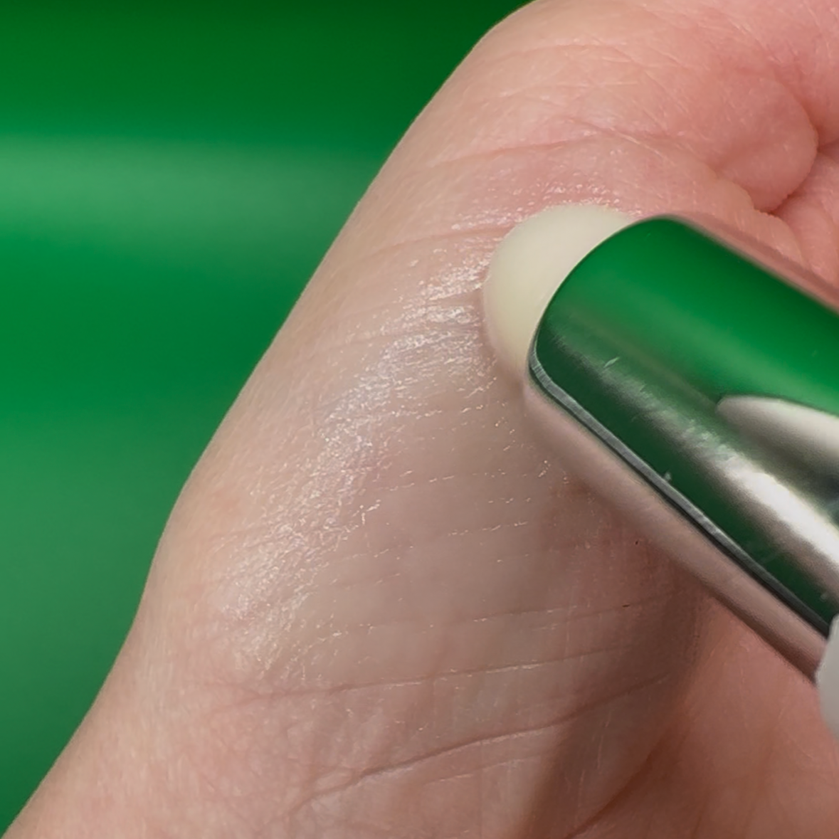 Clear vegan lip balm applied on hand for smooth, hydrated skin against green background