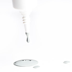 White nail polish brush dripping grey vegan nail lacquer onto a white surface