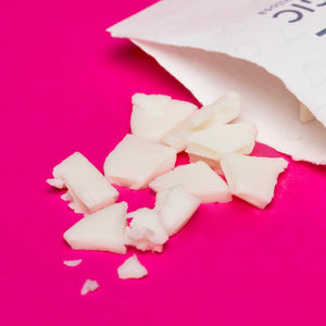 White cosmetic wax chips spilling from paper packaging on a bright pink background