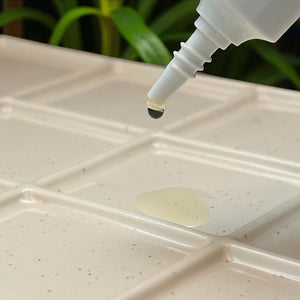 Dropper dispensing clear serum onto cream mixing palette, DIY natural skincare concept