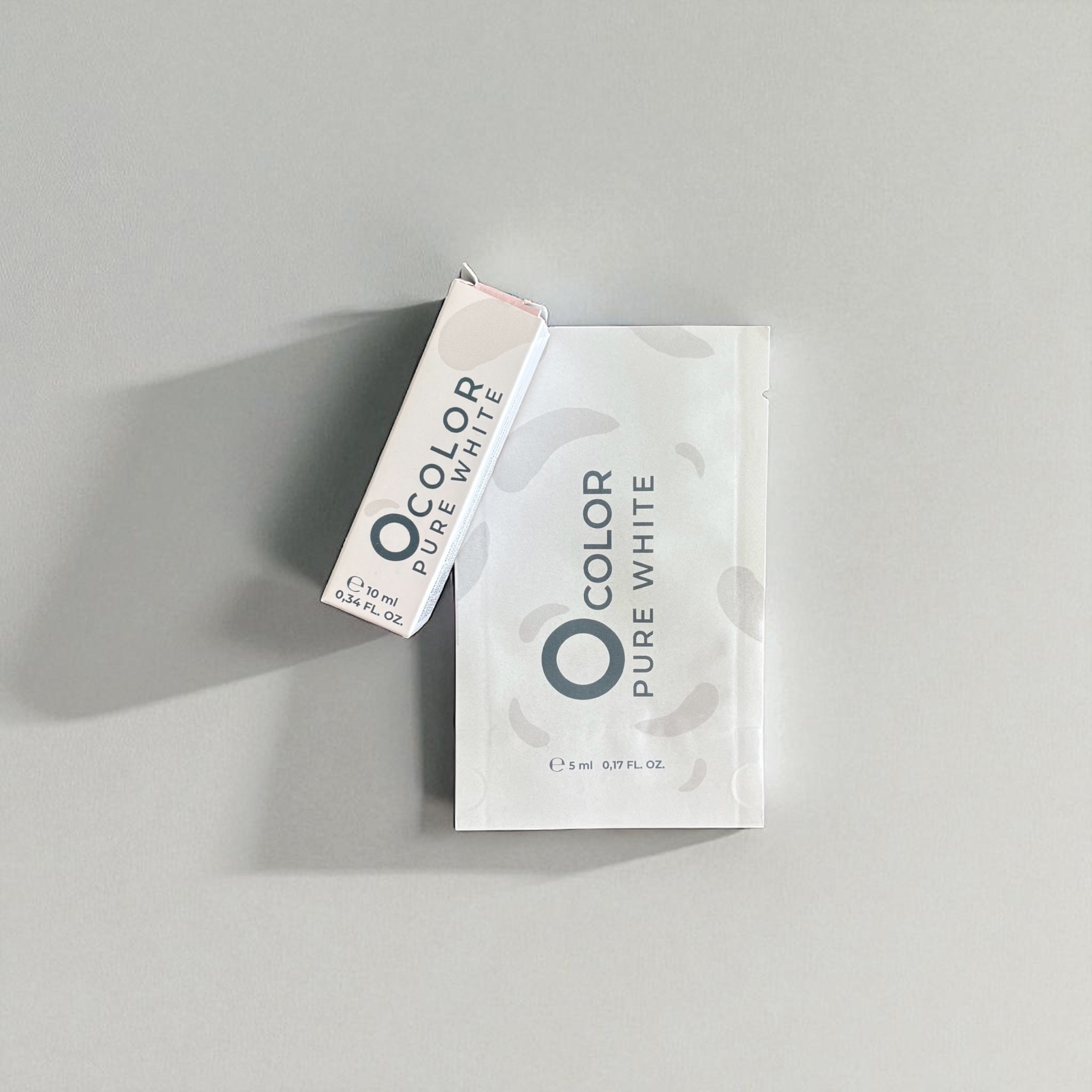 Minimalist packaging for O Color Pure White hair or brow dye with sachet and box on gray background