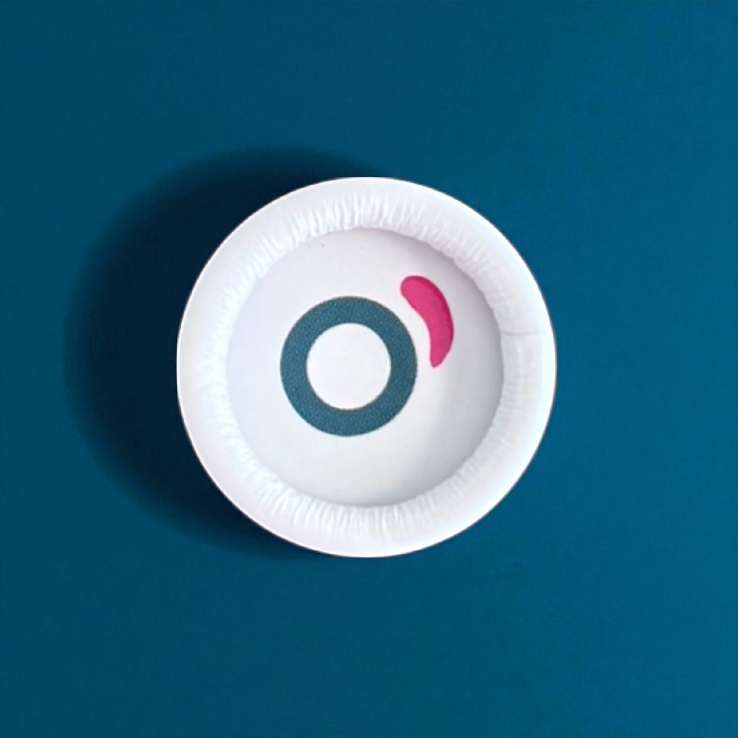 White round cosmetic container lid with teal and pink logo on blue background