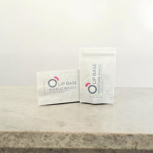Two Ophelier lip care base sachets on a marble surface, labeled Shield Boost and Moisture Magic.