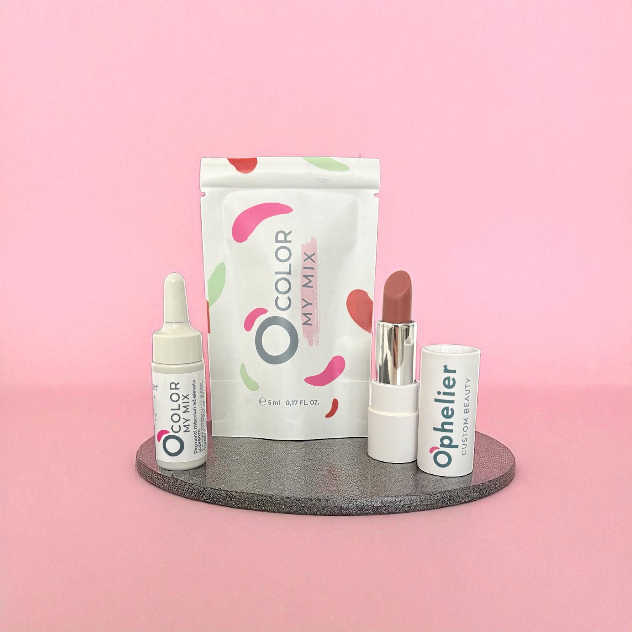 Natural vegan lipstick, serum dropper, and mixing kit on a gray tray with pink background