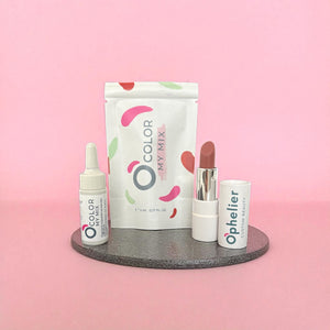 Natural vegan lipstick, serum dropper, and mixing kit on a gray tray with pink background